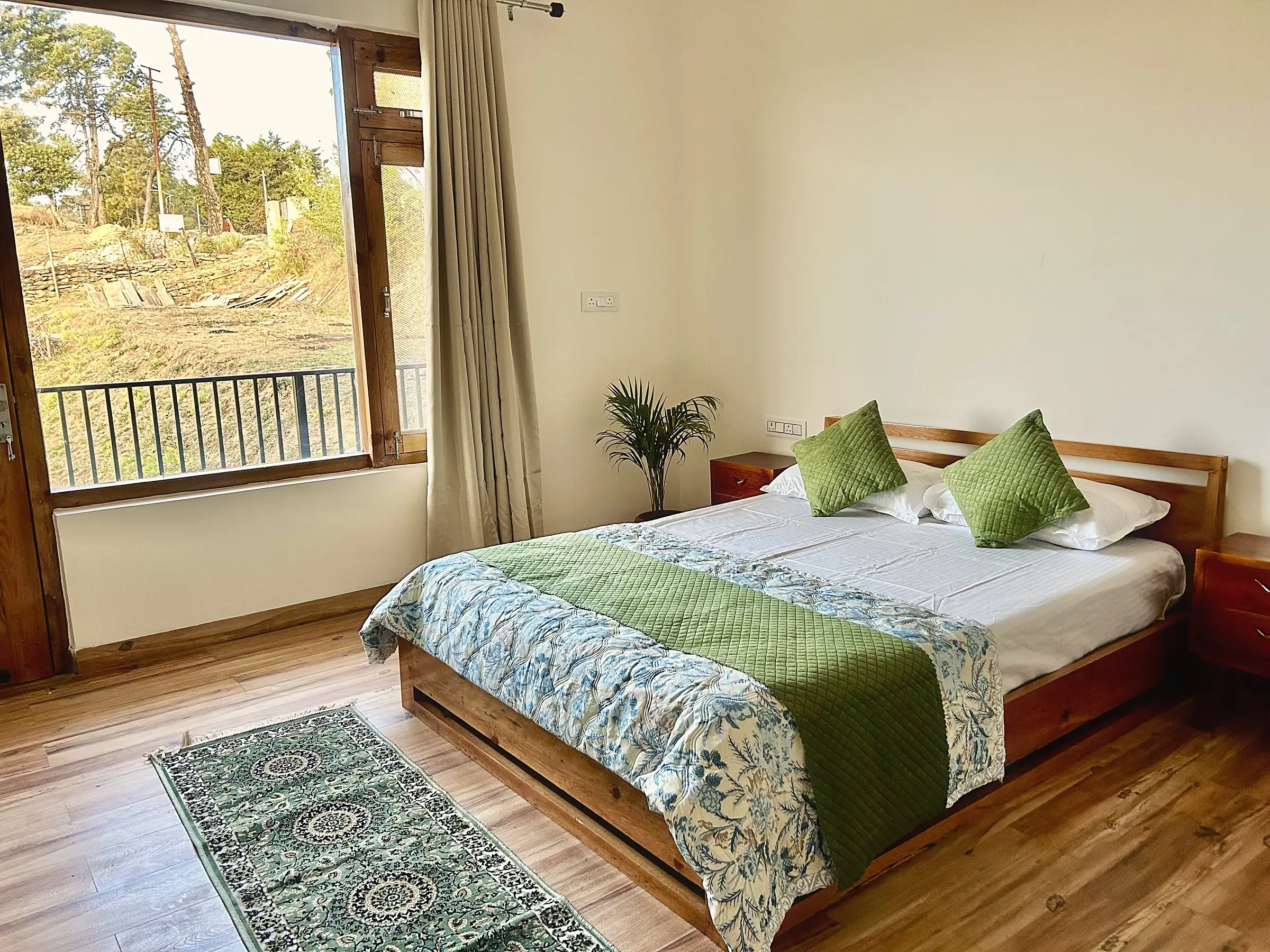 A bed with green cushions beside a window onto pines and a railing