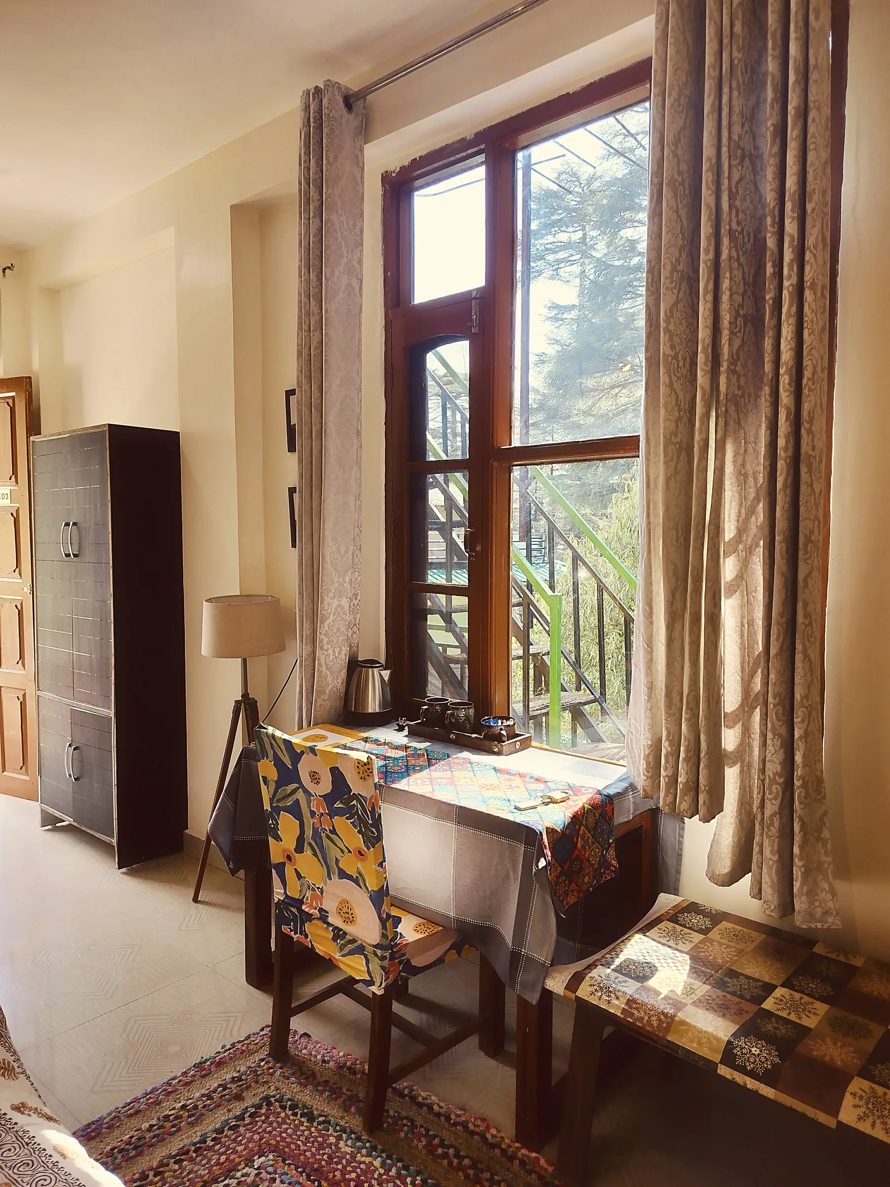 A small table, chair and kettle by the window, next to a wardrobe