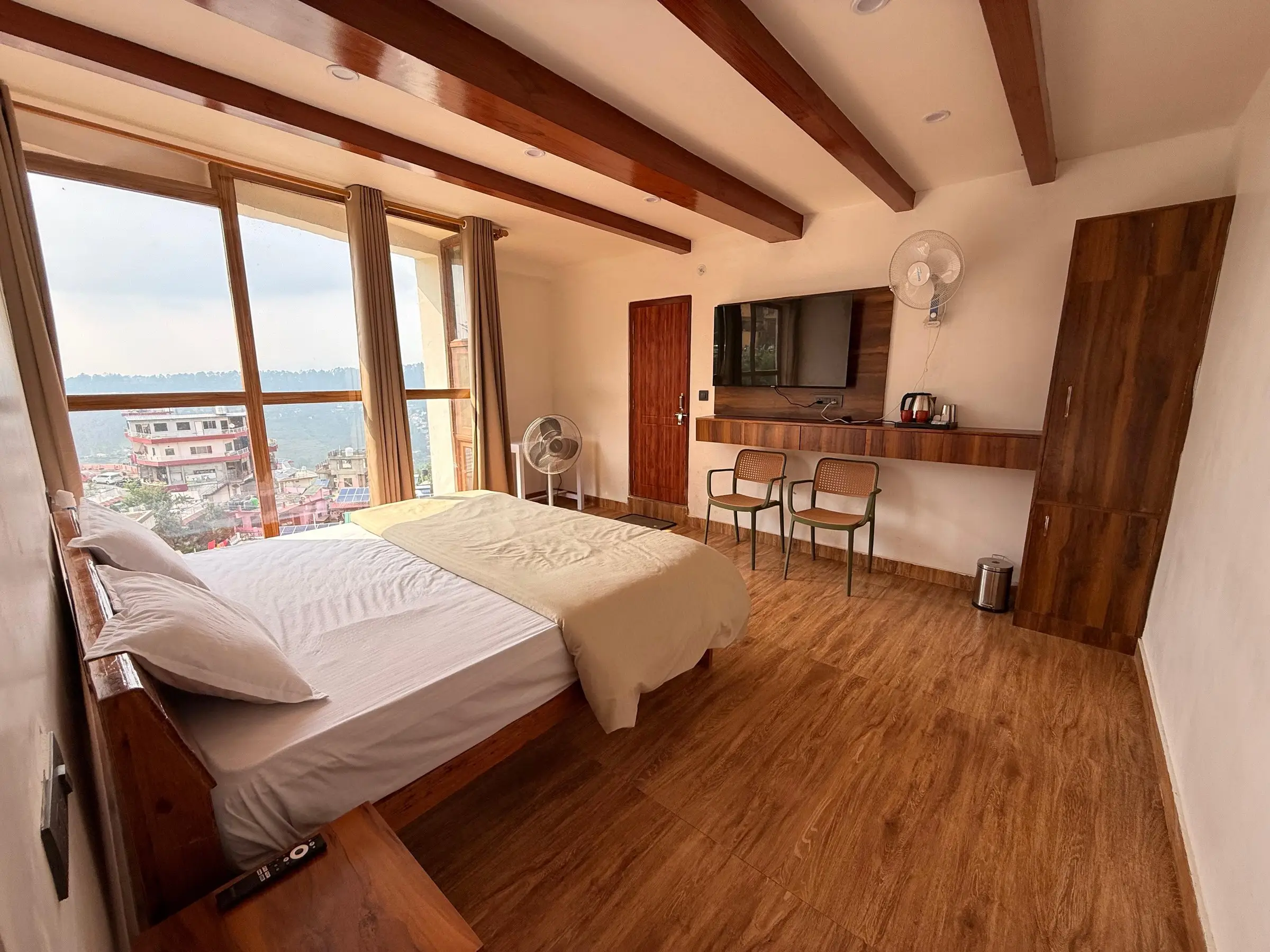 A bedroom with timber beams, a tall window and rooftops beyond