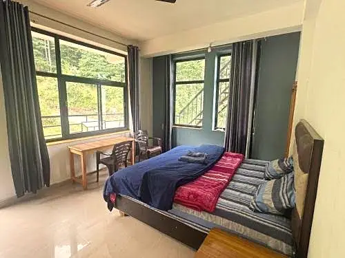 The room, with a double bed, a wooden desk and windows onto trees