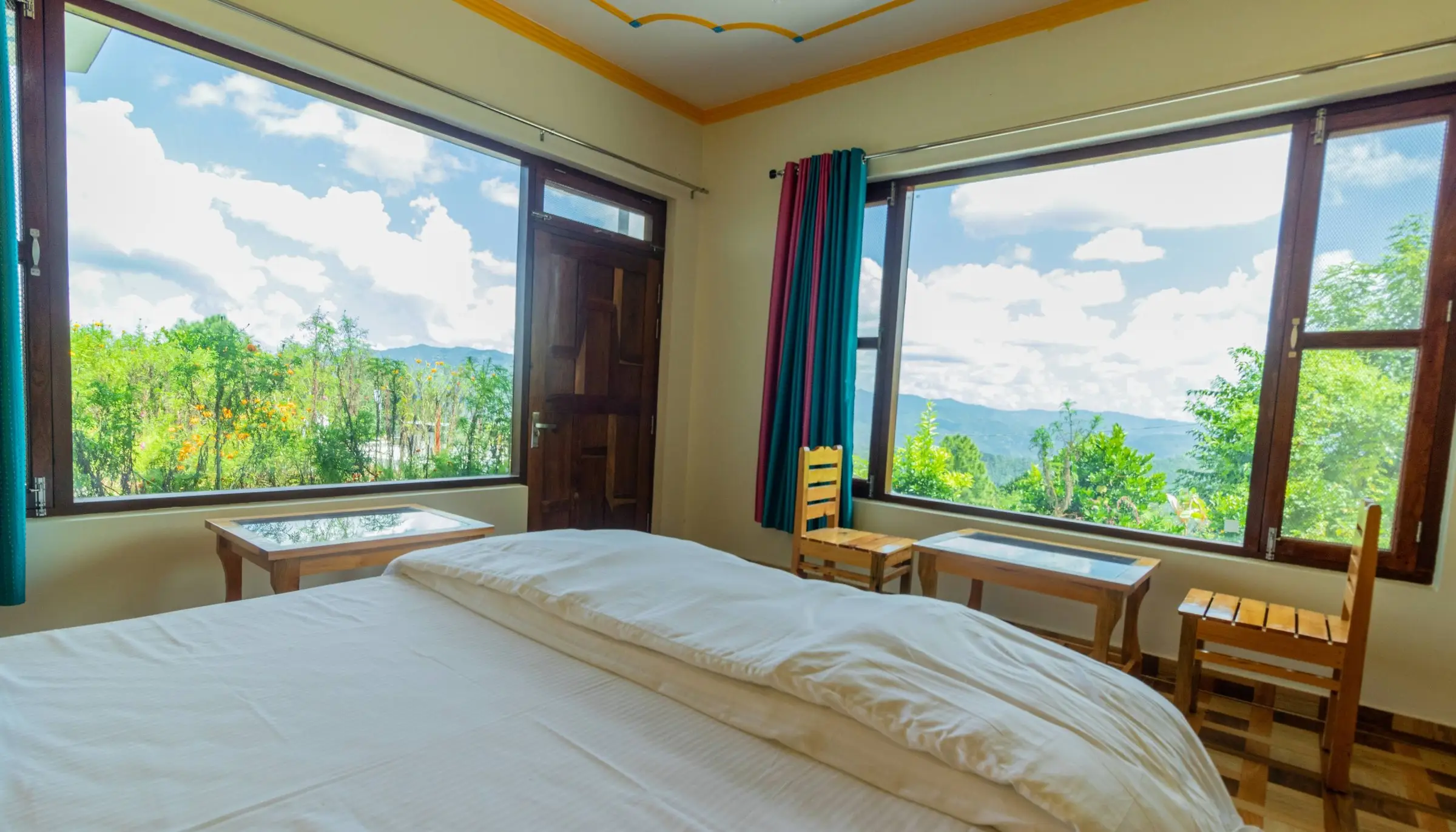 The bed with two big windows looking onto trees and hills