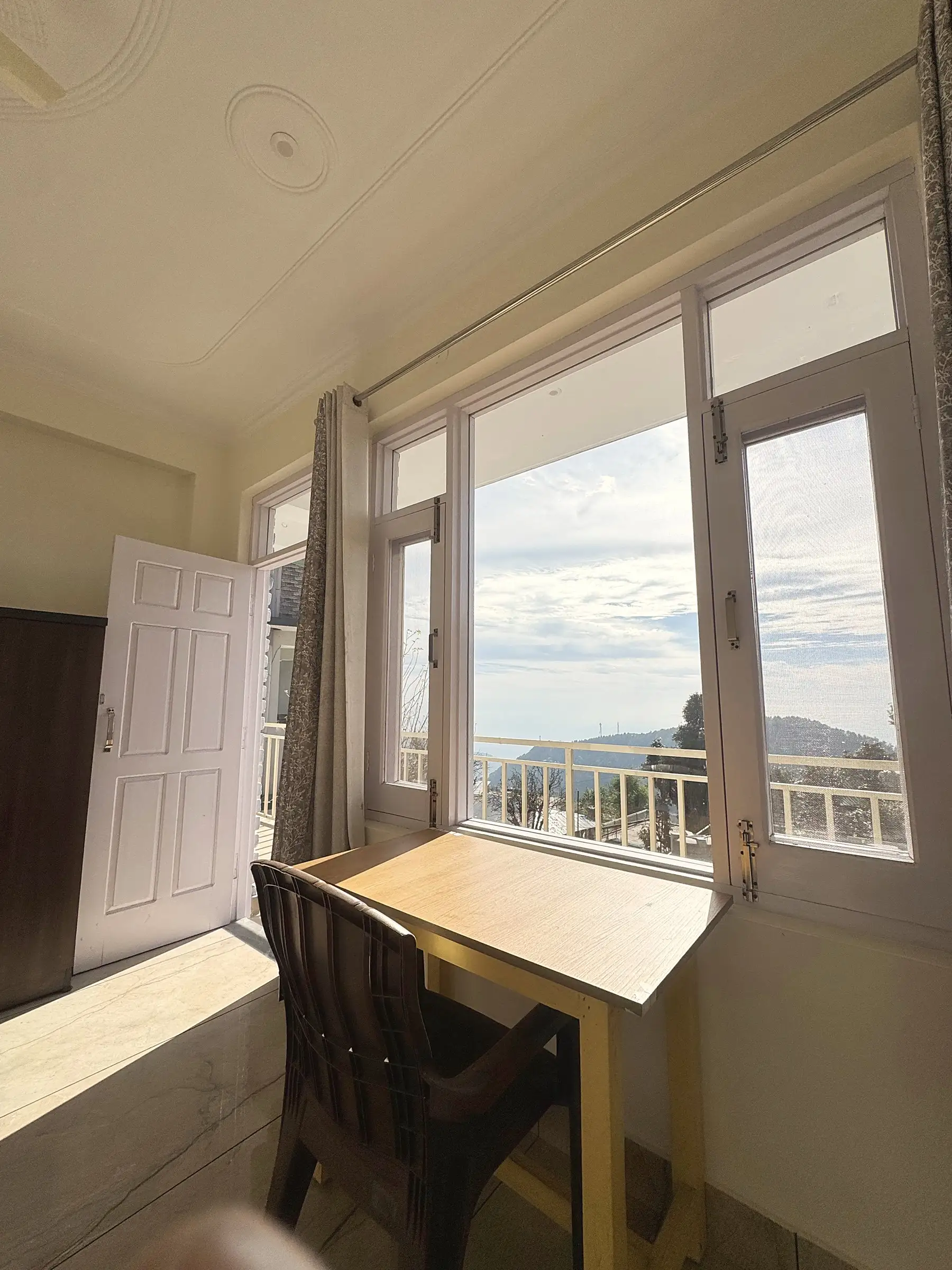 The desk at the window, looking out over the balcony rail to the hills