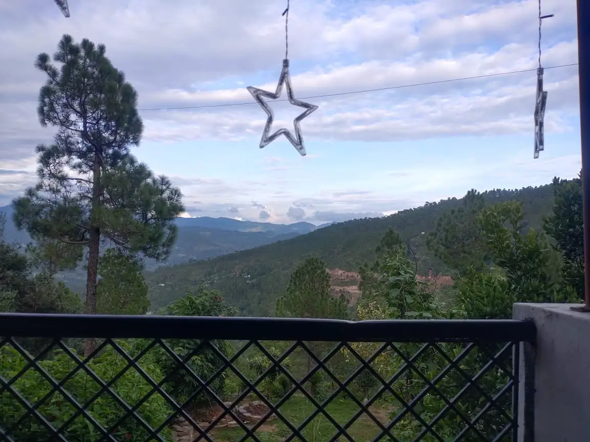 A balcony railing with pines and forested ridges beyond