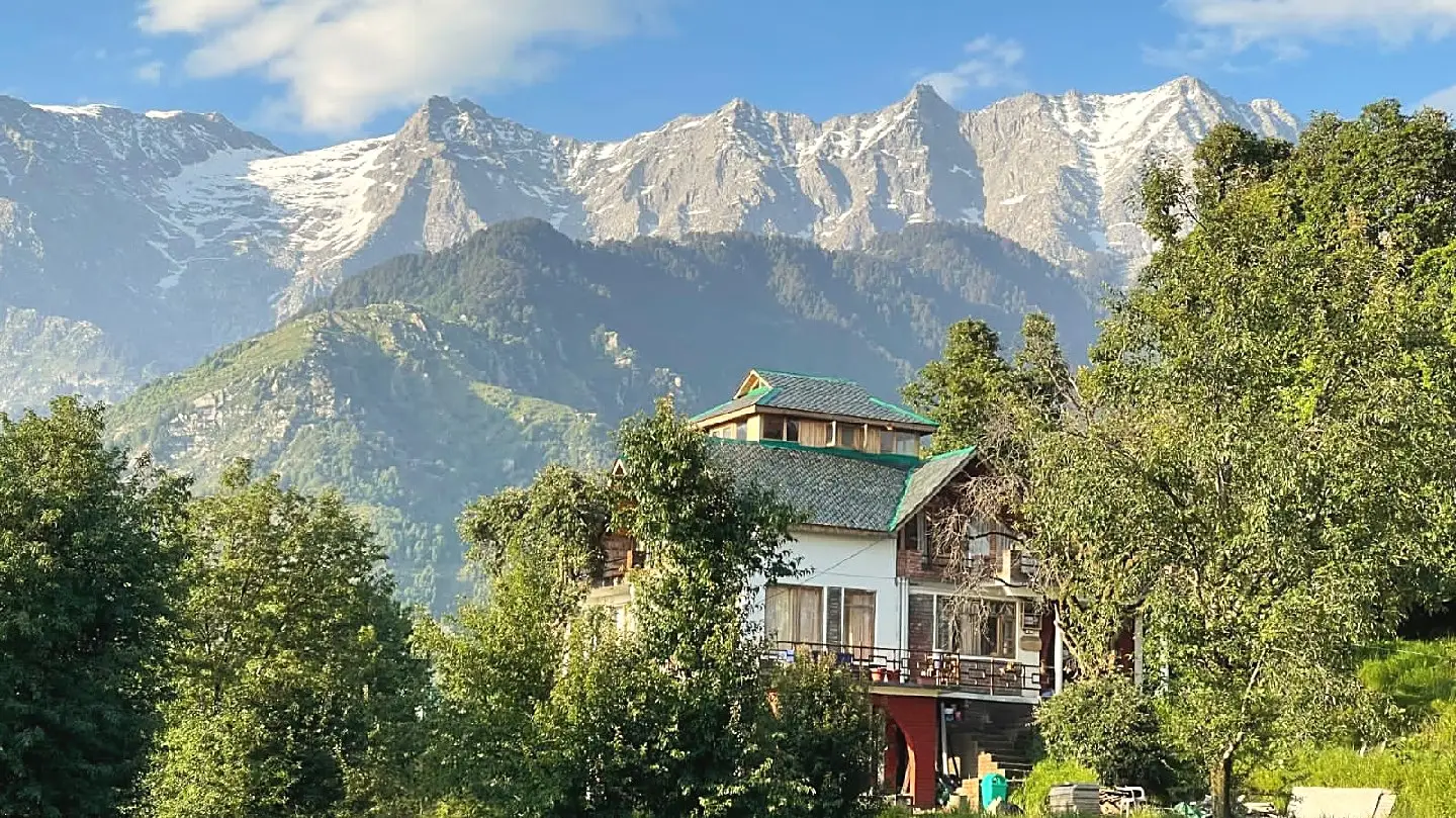 The house among trees, with snow-covered peaks behind it