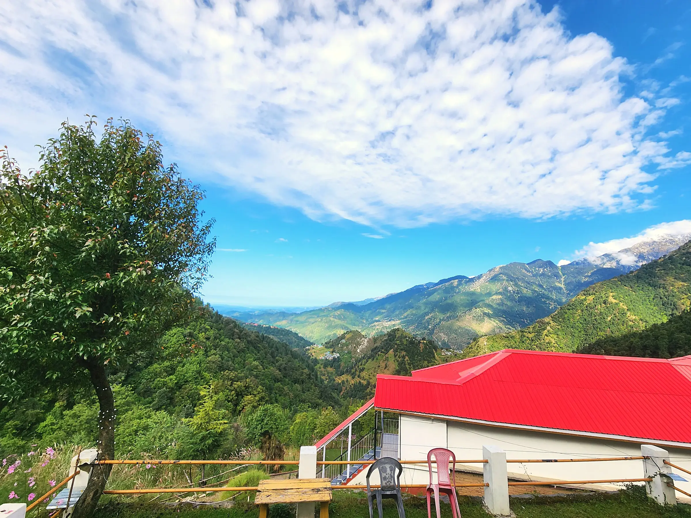 A red-roofed building and forested ridges under a wide blue sky