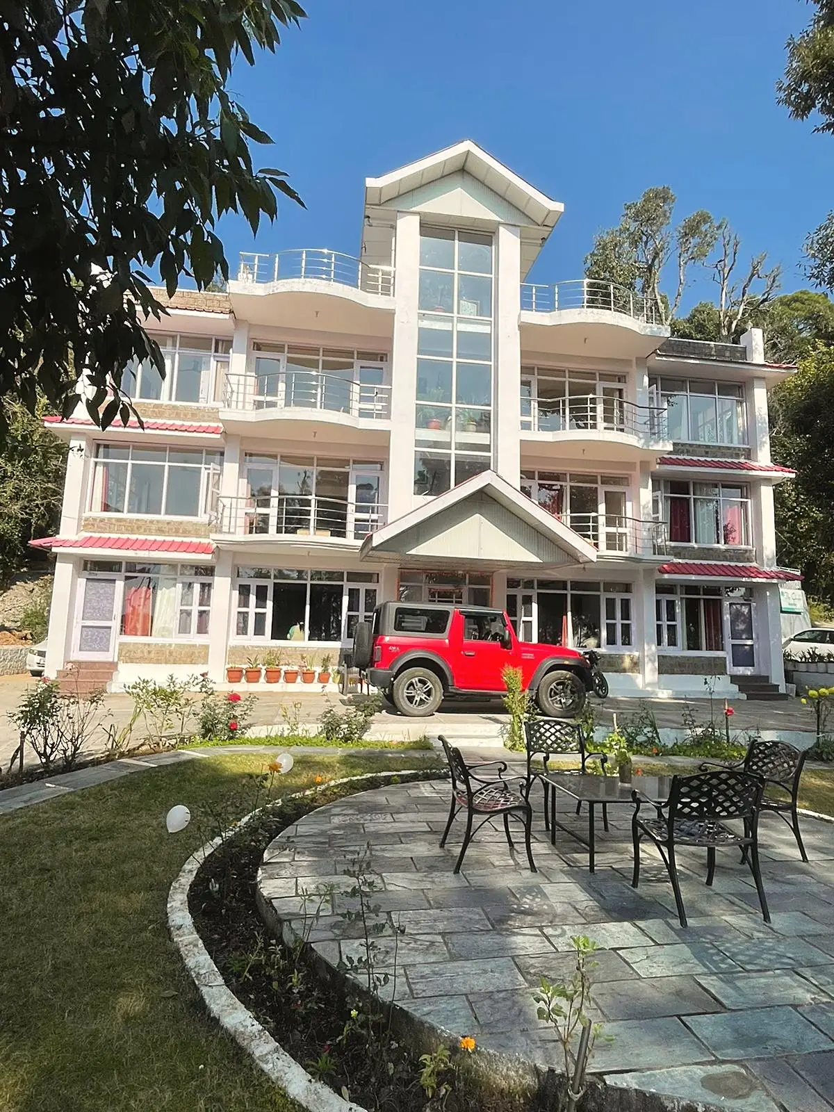 The white building from the garden, with a stone patio and metal chairs