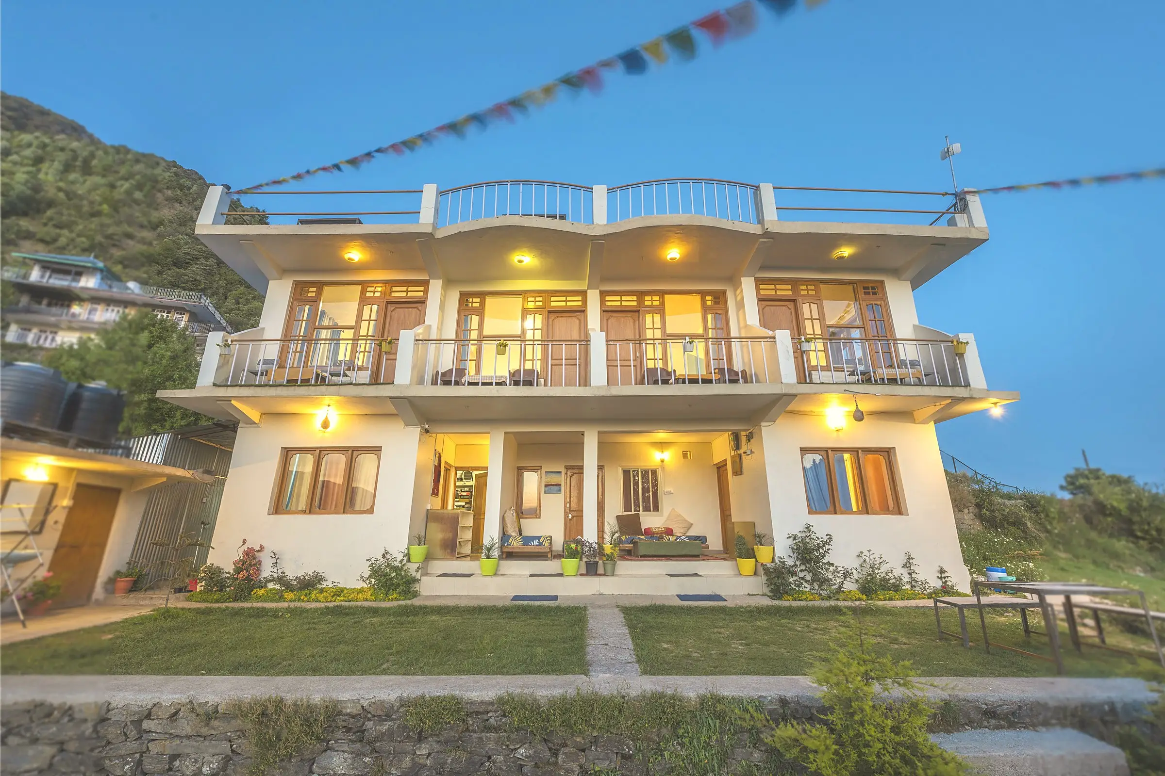 The two-floor building at dusk, with lit balconies and prayer flags