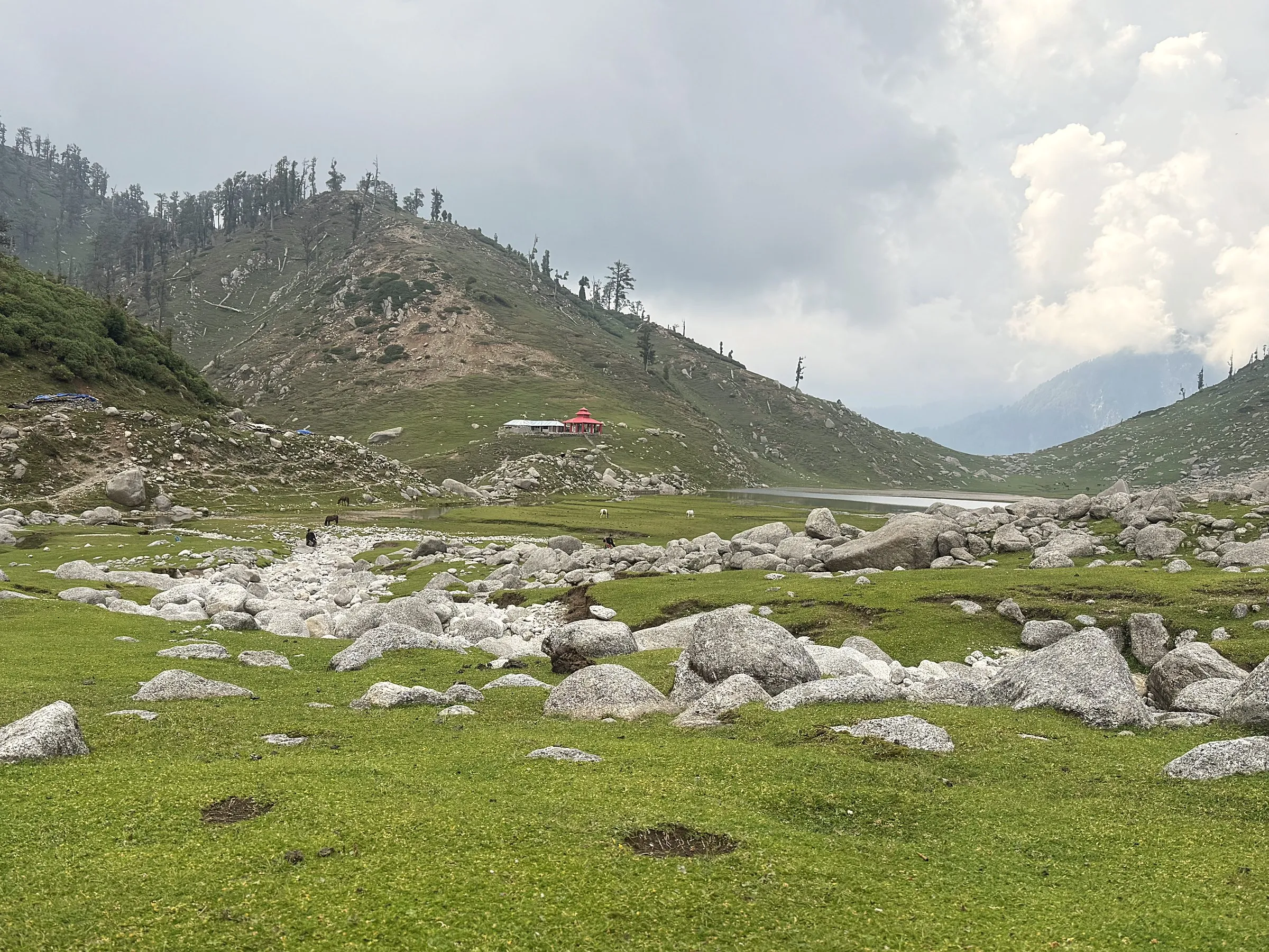 An open meadow of boulders, with a small red-roofed building and a lake beyond