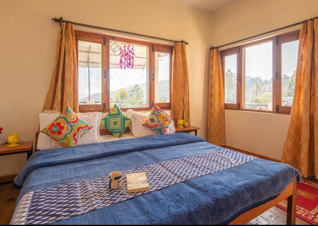 A blue-covered double bed under two windows, with a mug and a book