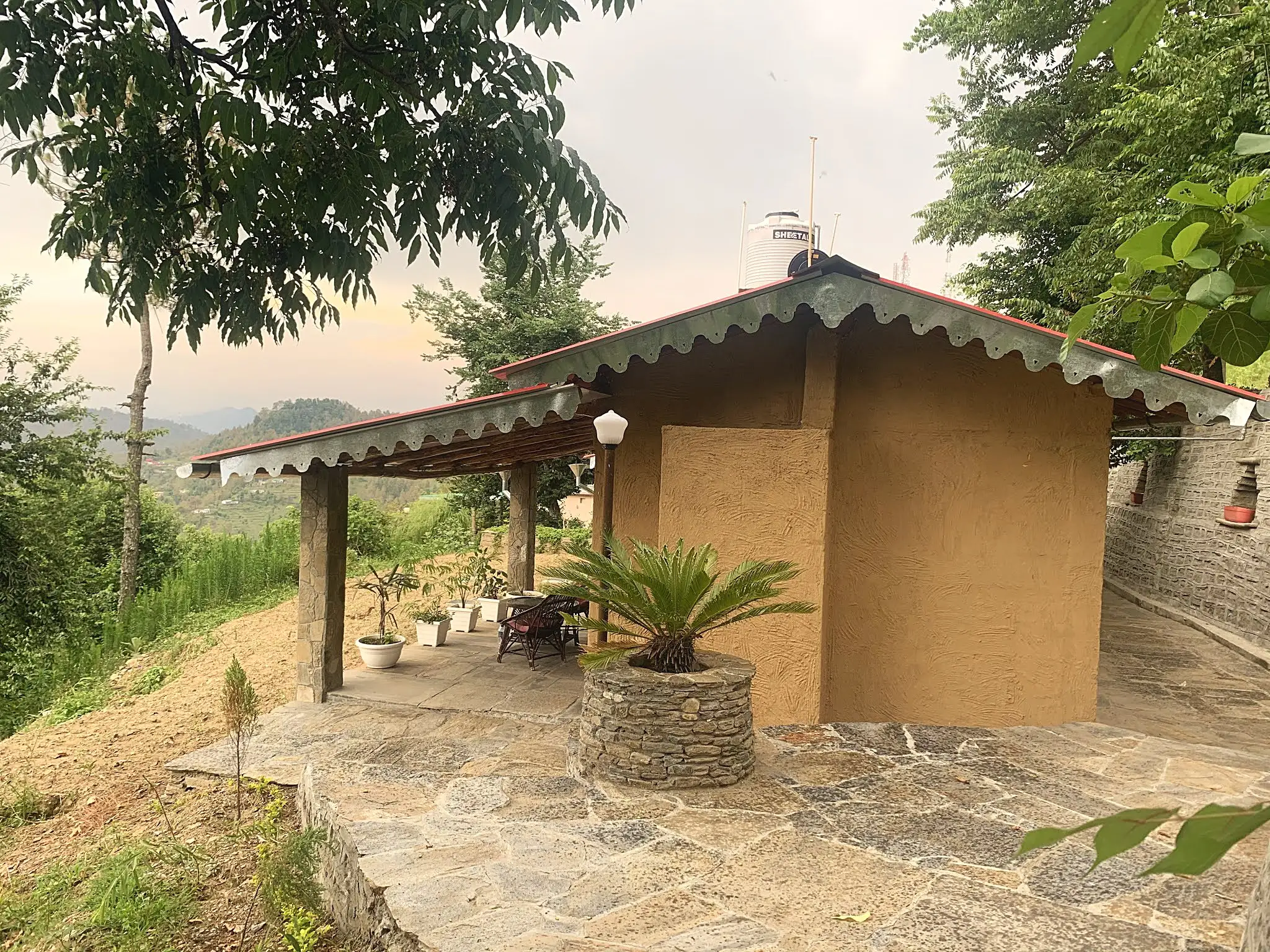 A single-storey mud-walled cottage with a covered porch and a stone patio