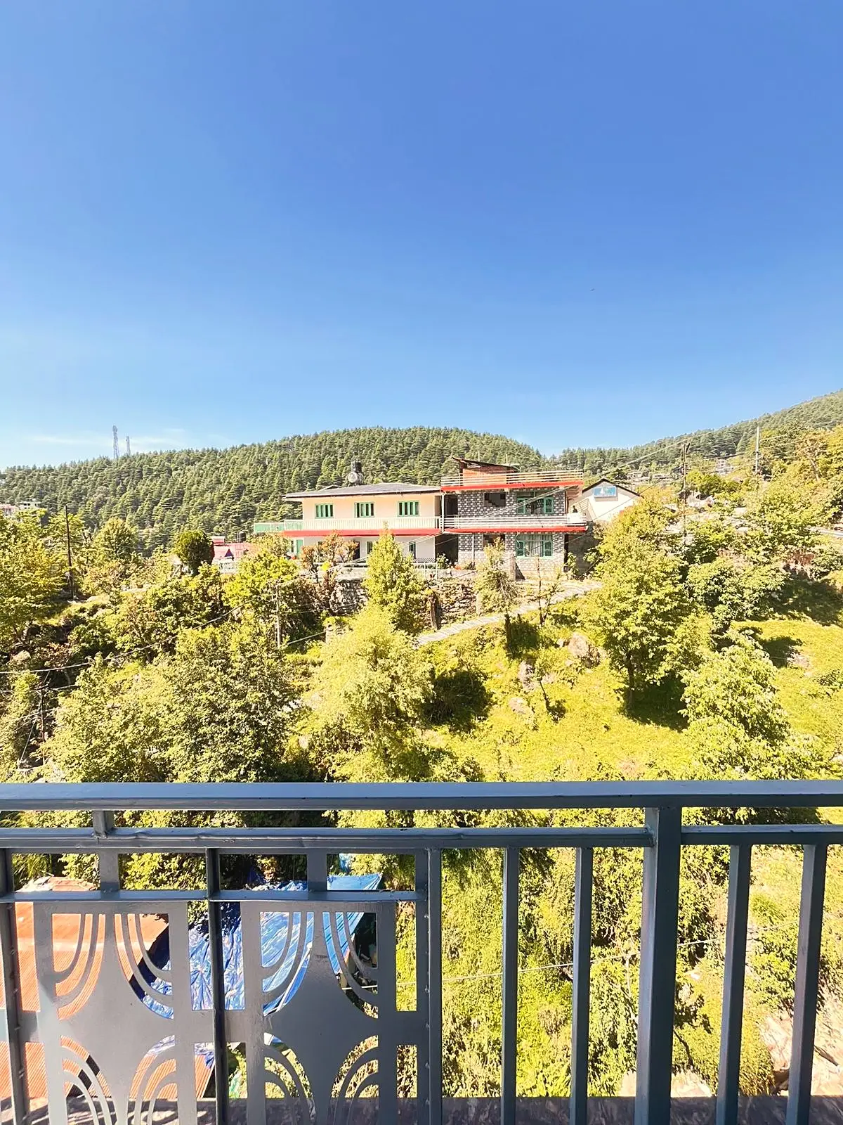 The view over a balcony rail to trees, houses and a wooded hill