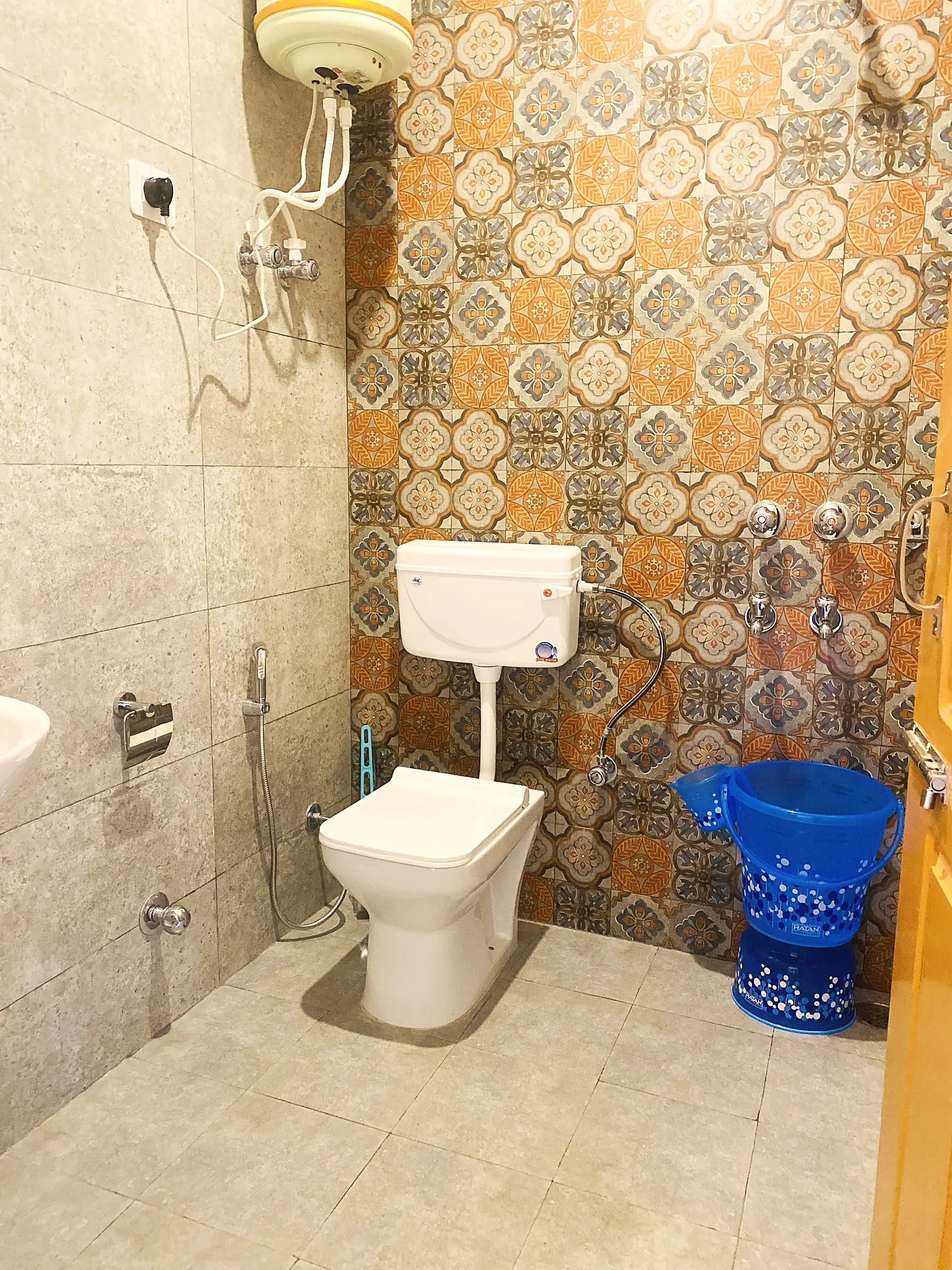 The bathroom, with tiled walls, a wall-mounted water heater and a hand shower