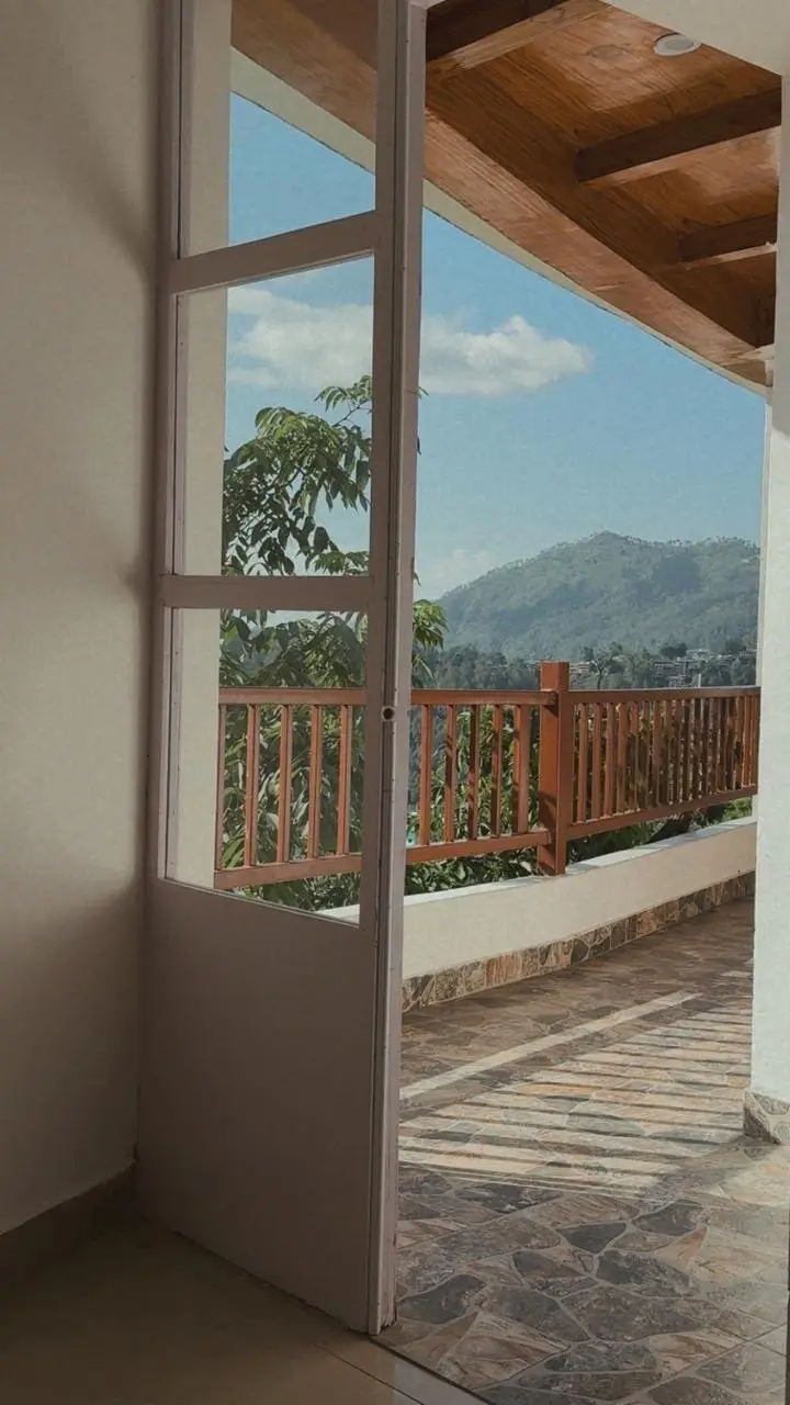 An open glazed door onto a stone balcony facing a green hill