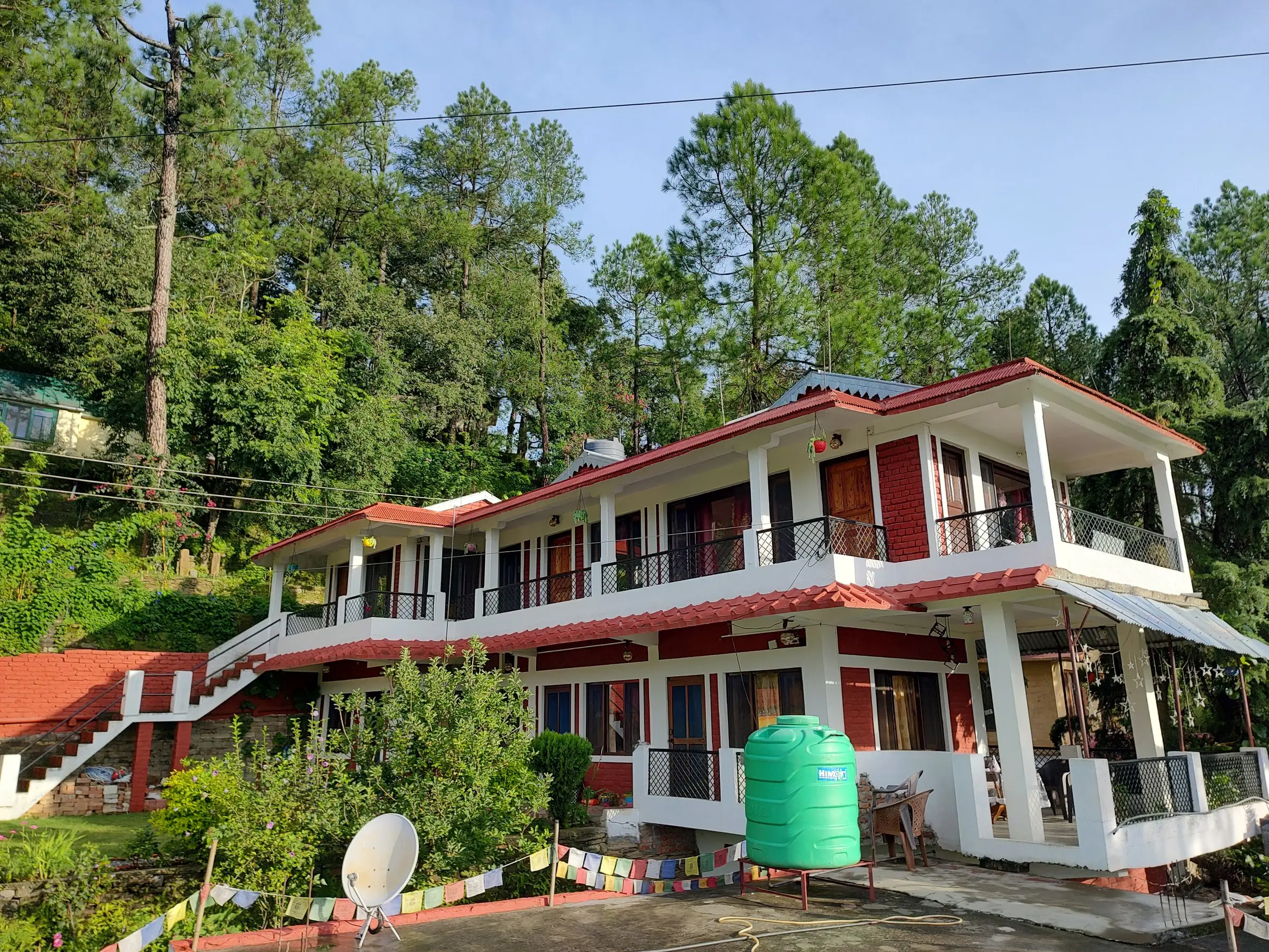 The red-roofed house with balconies, among pines and prayer flags