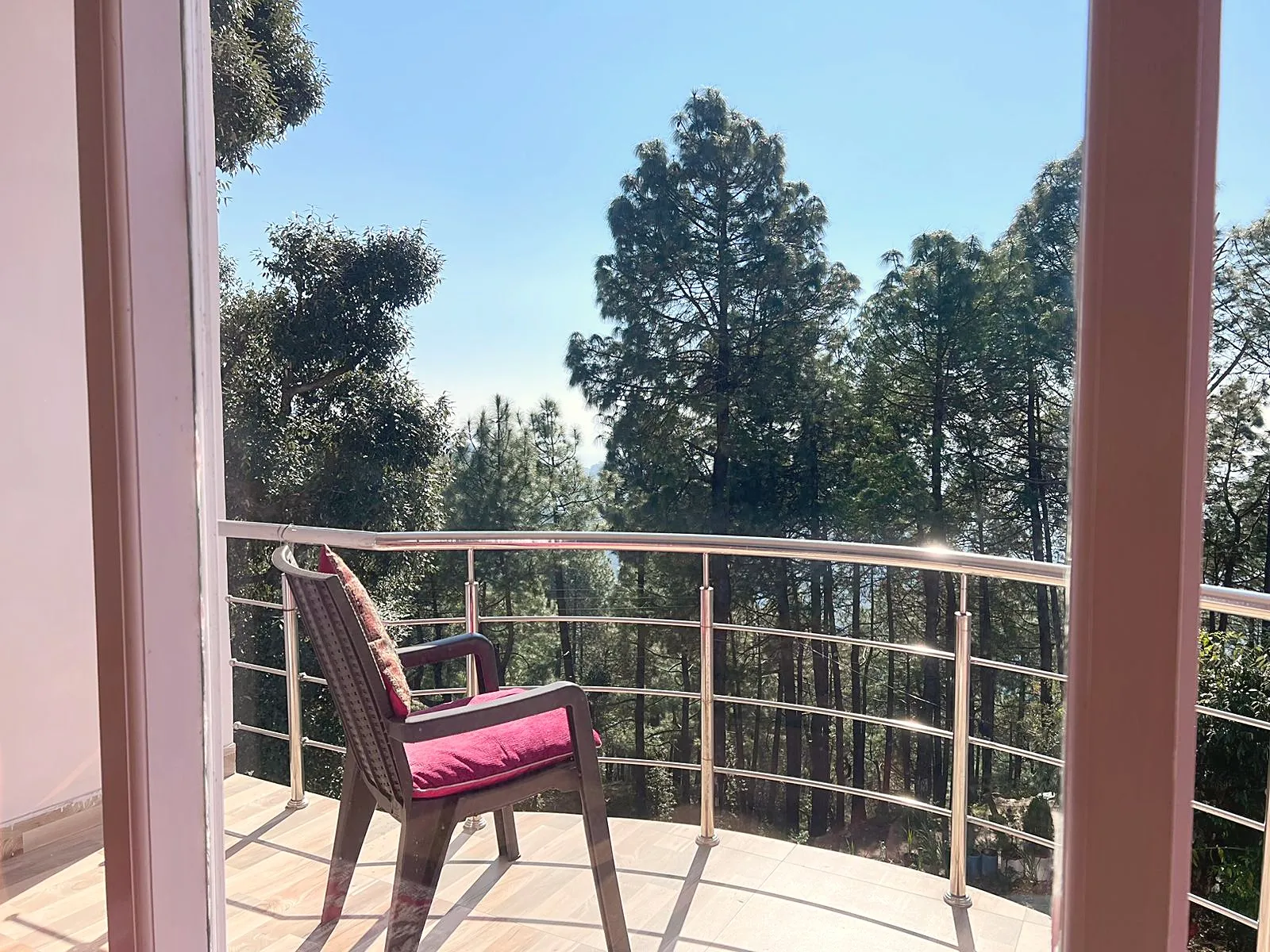 A balcony chair with red cushions, facing tall pines