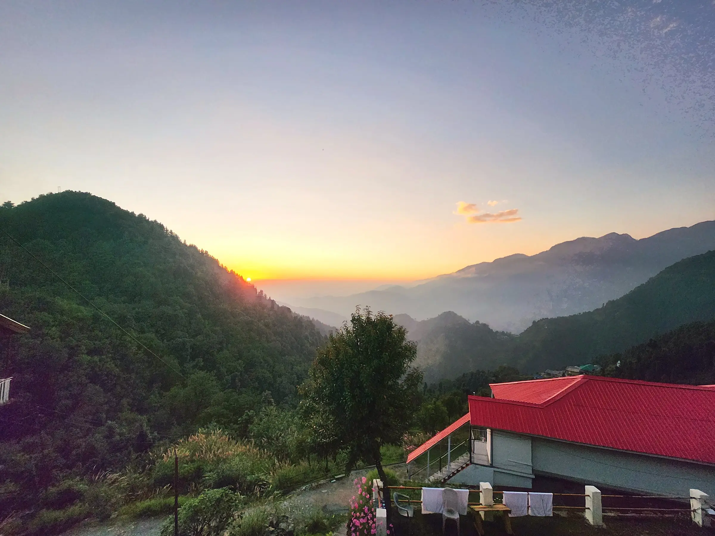 Sunset over a dark forested ridge, with a red roof in the foreground