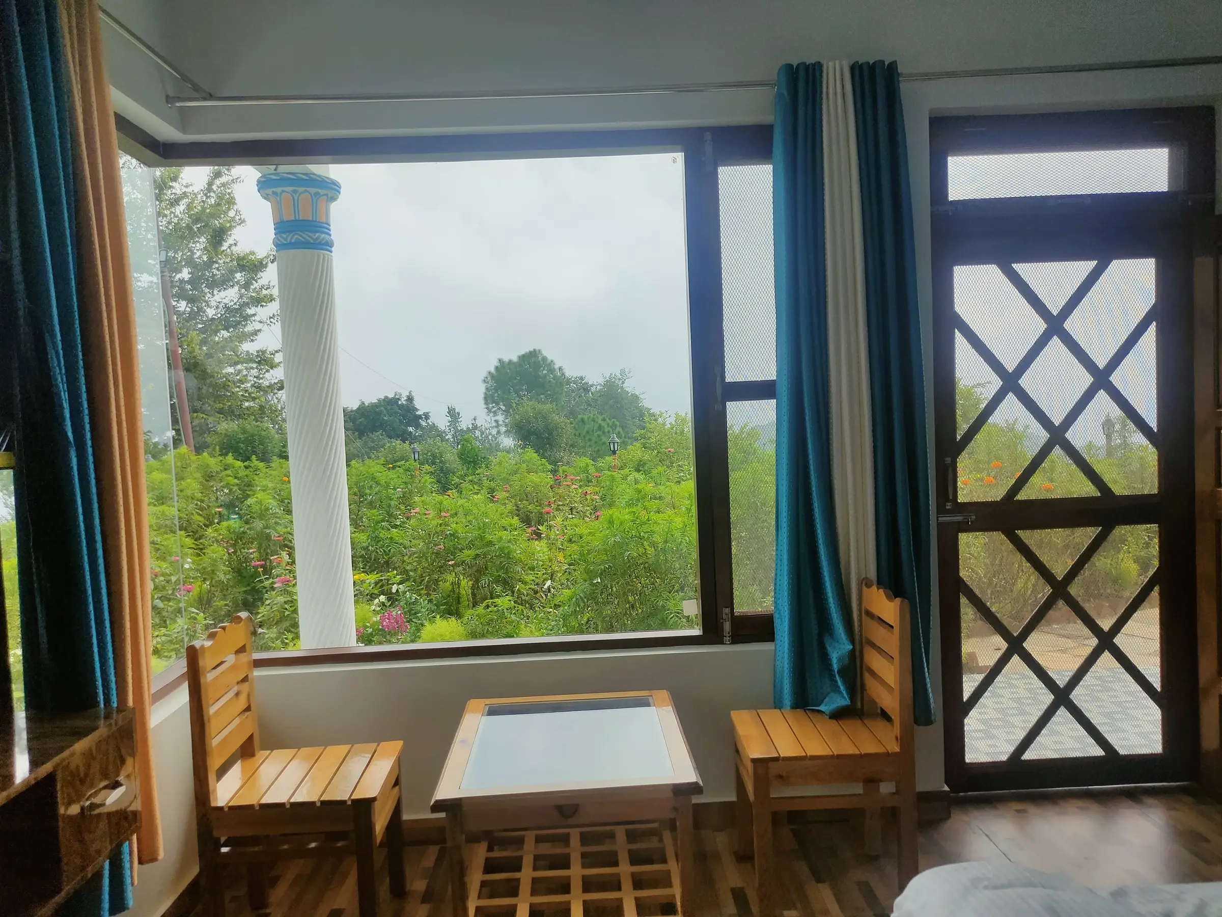 A small table and two wooden chairs at a window onto the garden