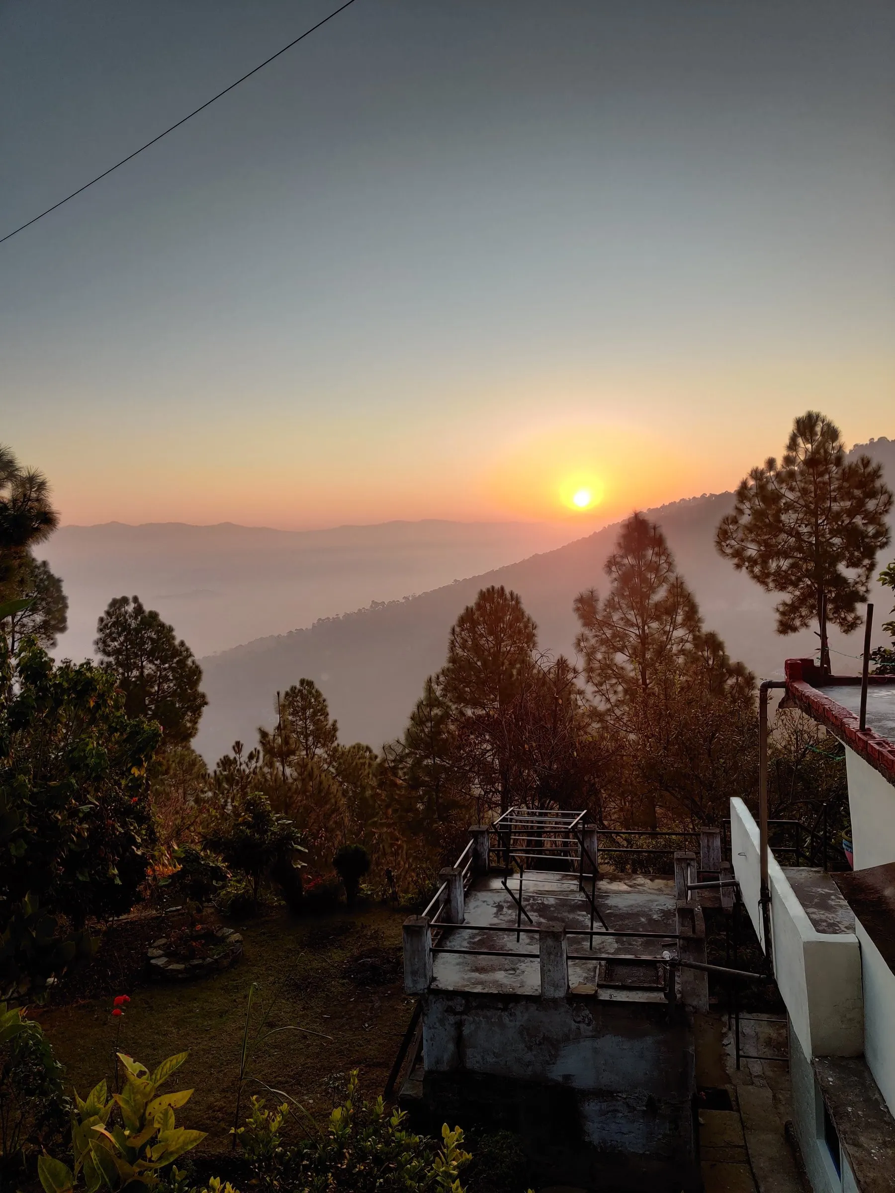The sun setting behind hazy ridges, seen from above a rooftop