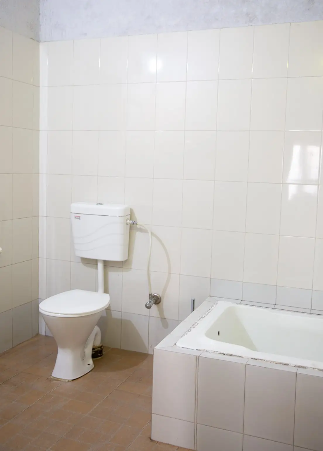 A white-tiled bathroom with a toilet and a bathtub