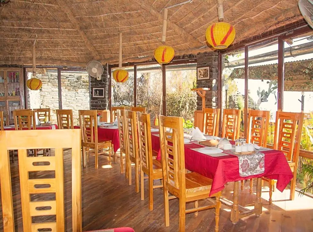 A thatch-roofed dining hall with wooden chairs and red tablecloths