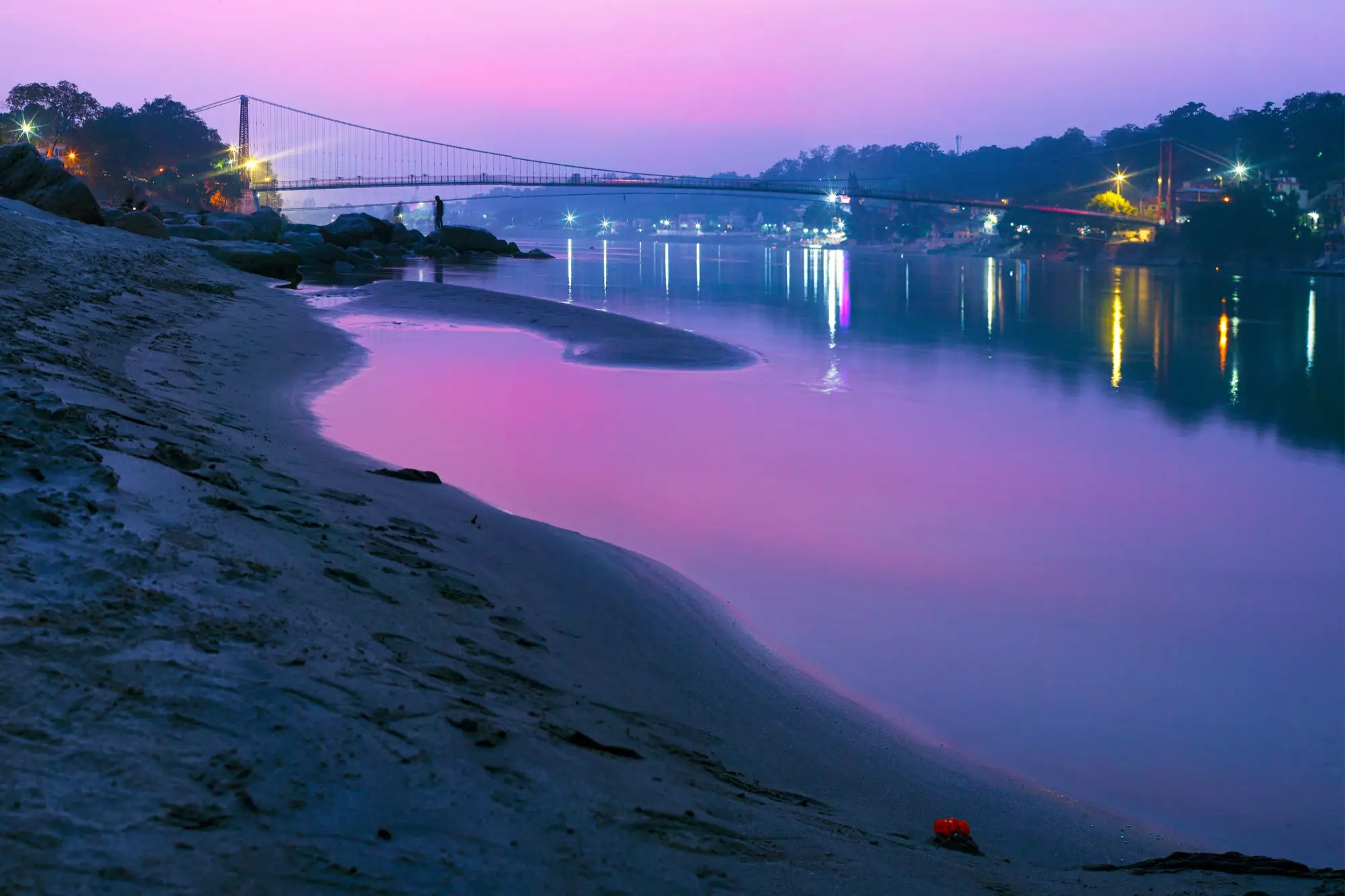 The Ganga at dusk at Rishikesh under a purple sky, with a suspension bridge lit across the river