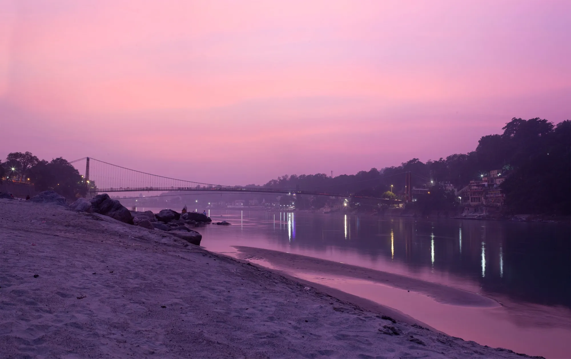 The Ganga at Rishikesh under a pink evening sky, with lights along the bank