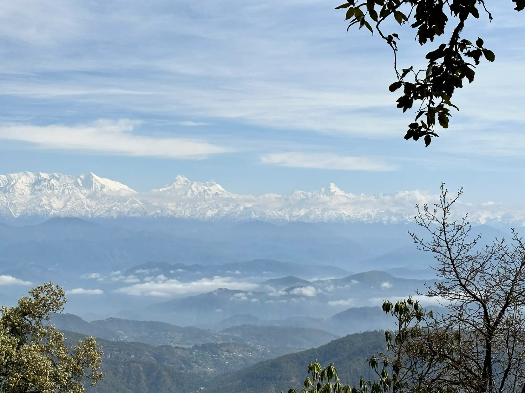 Snow peaks above layers of blue hills and cloud, seen from Binsar