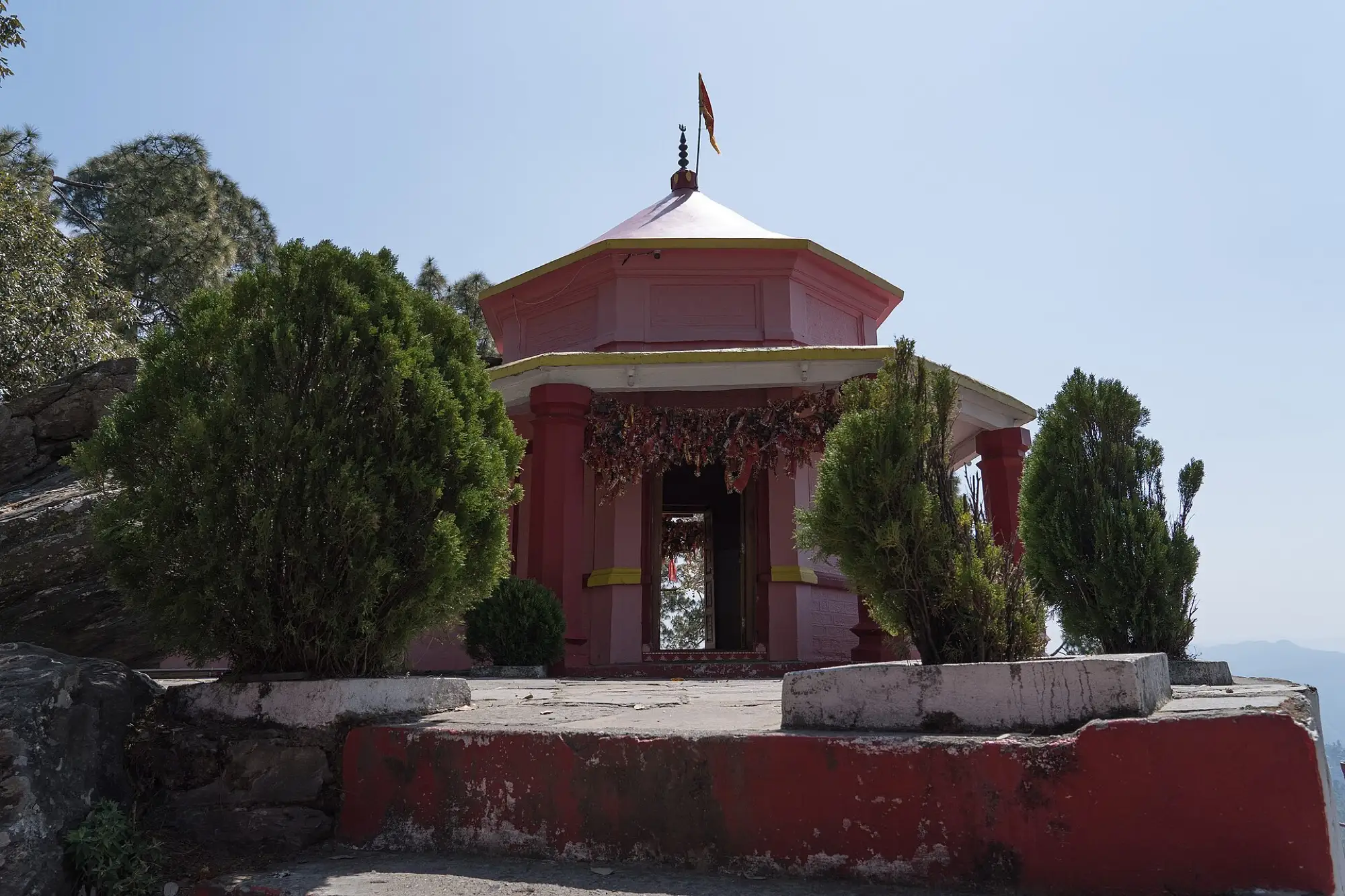 The pink and red octagonal Kasar Devi temple with a flag on its roof