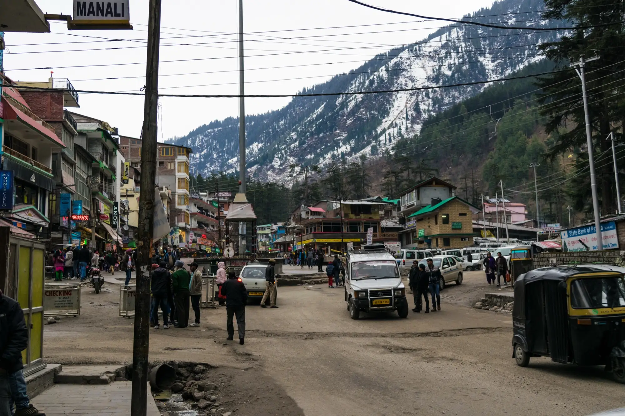 Mall Road in Manali with shops, parked jeeps and snowy slopes behind