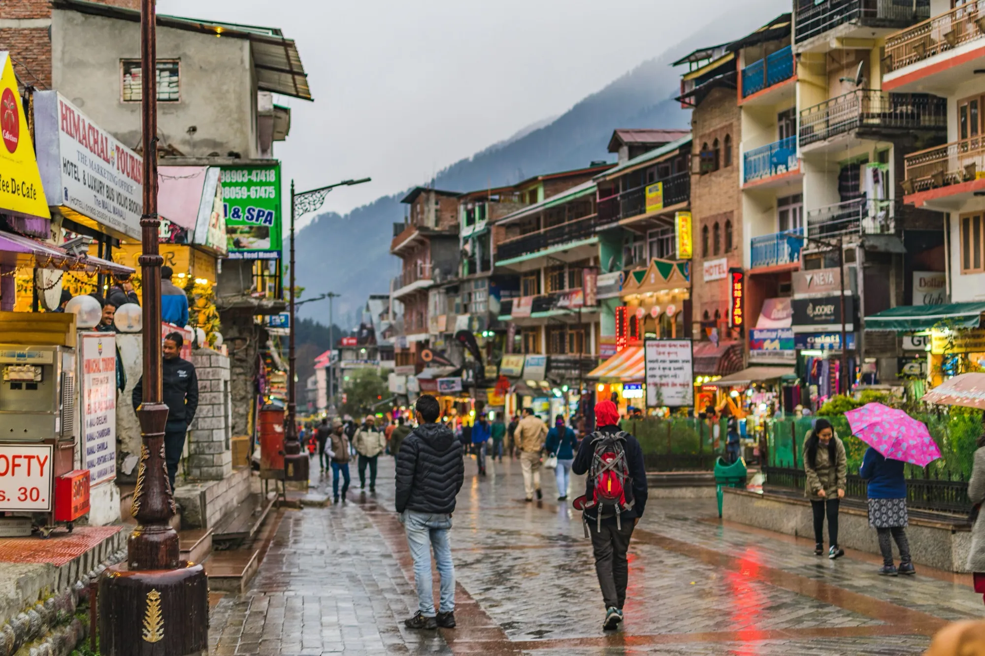 Mall Road in Manali on a wet day, with shops, signboards and people walking