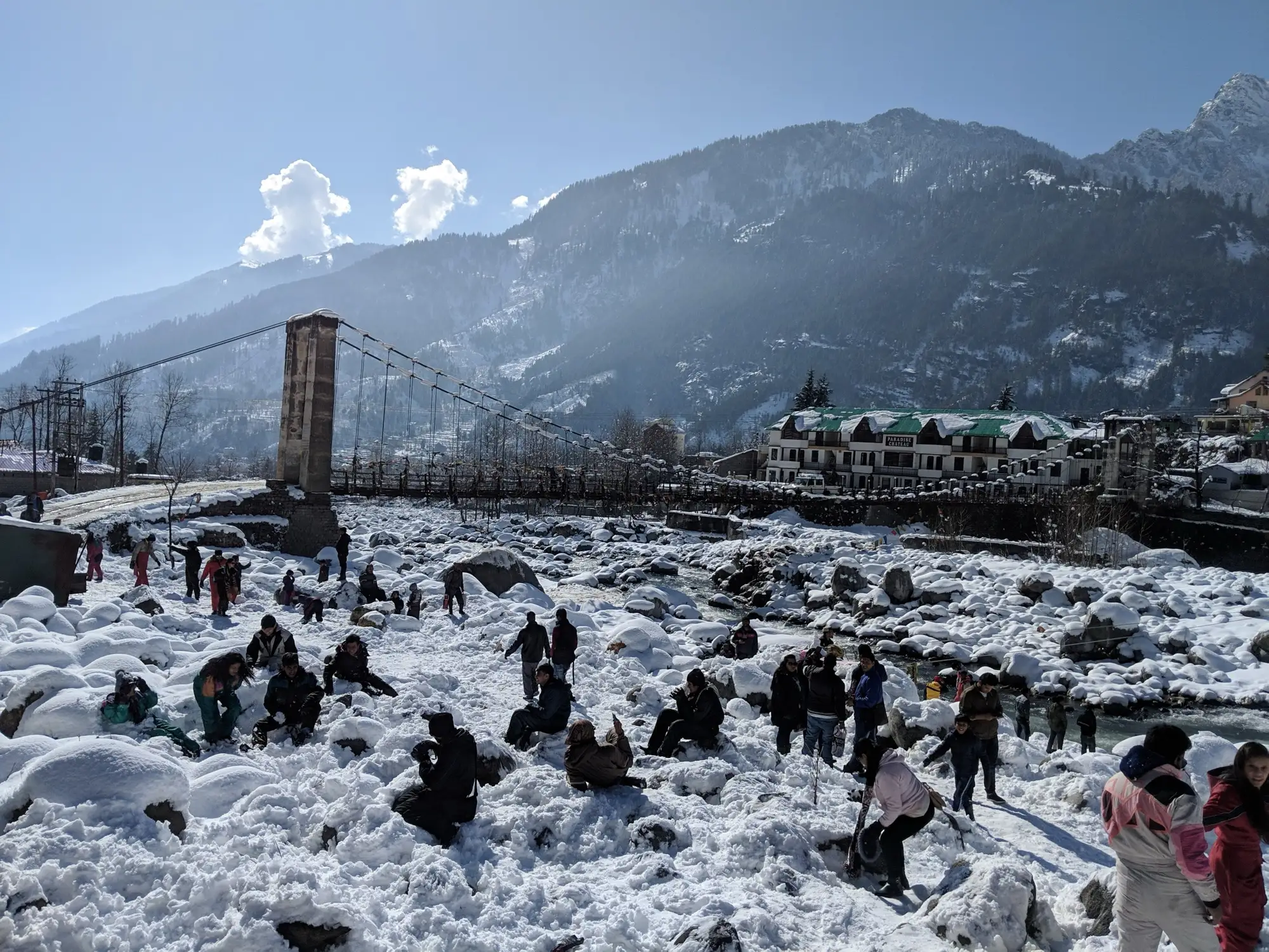 Manali buildings and a bridge with people playing in fresh snow