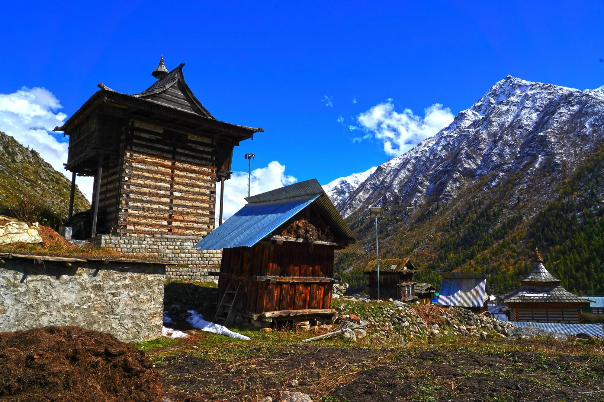 A timber tower and storehouses with a snow-dusted ridge behind, in Chitkul