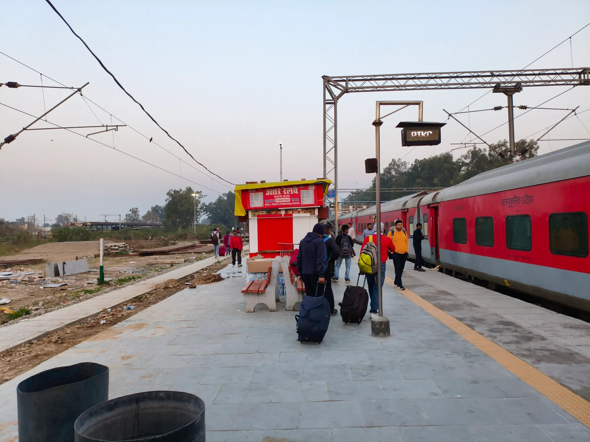 A red train at a platform at Pathankot Cantt station, with passengers and luggage