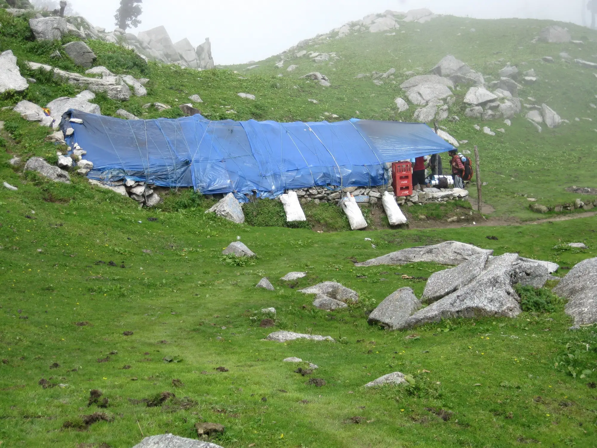 A tarpaulin-roofed tea stall on a green slope above Triund
