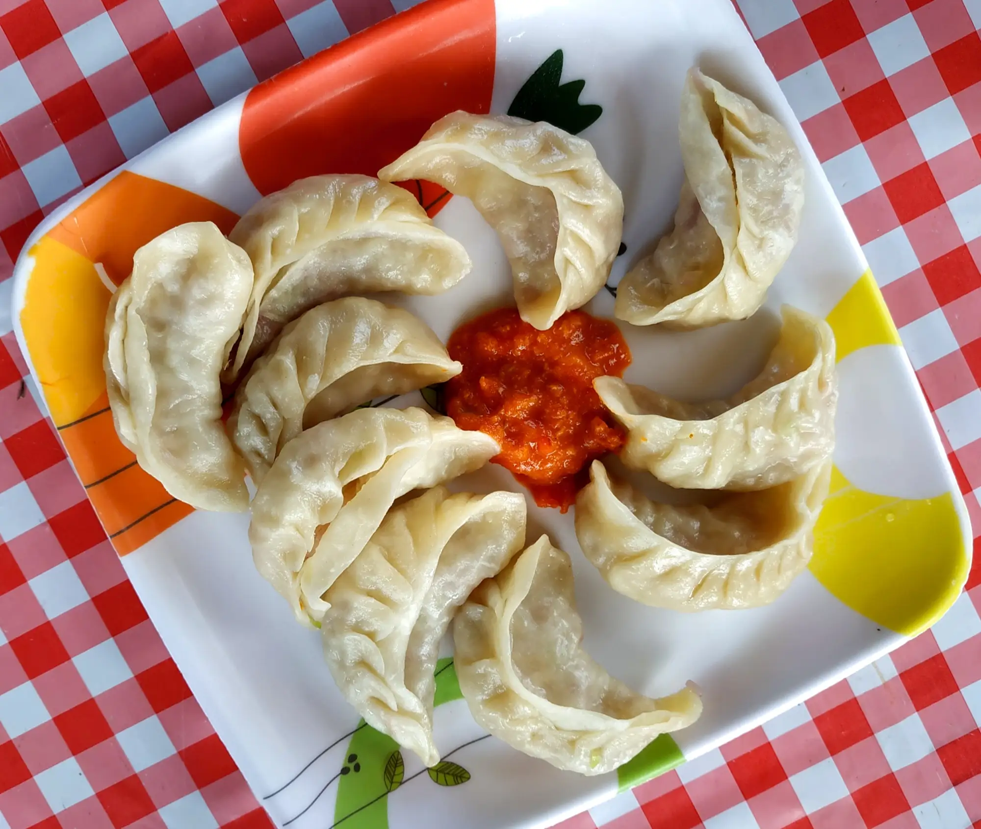 A plate of steamed momos around a spoonful of red chutney