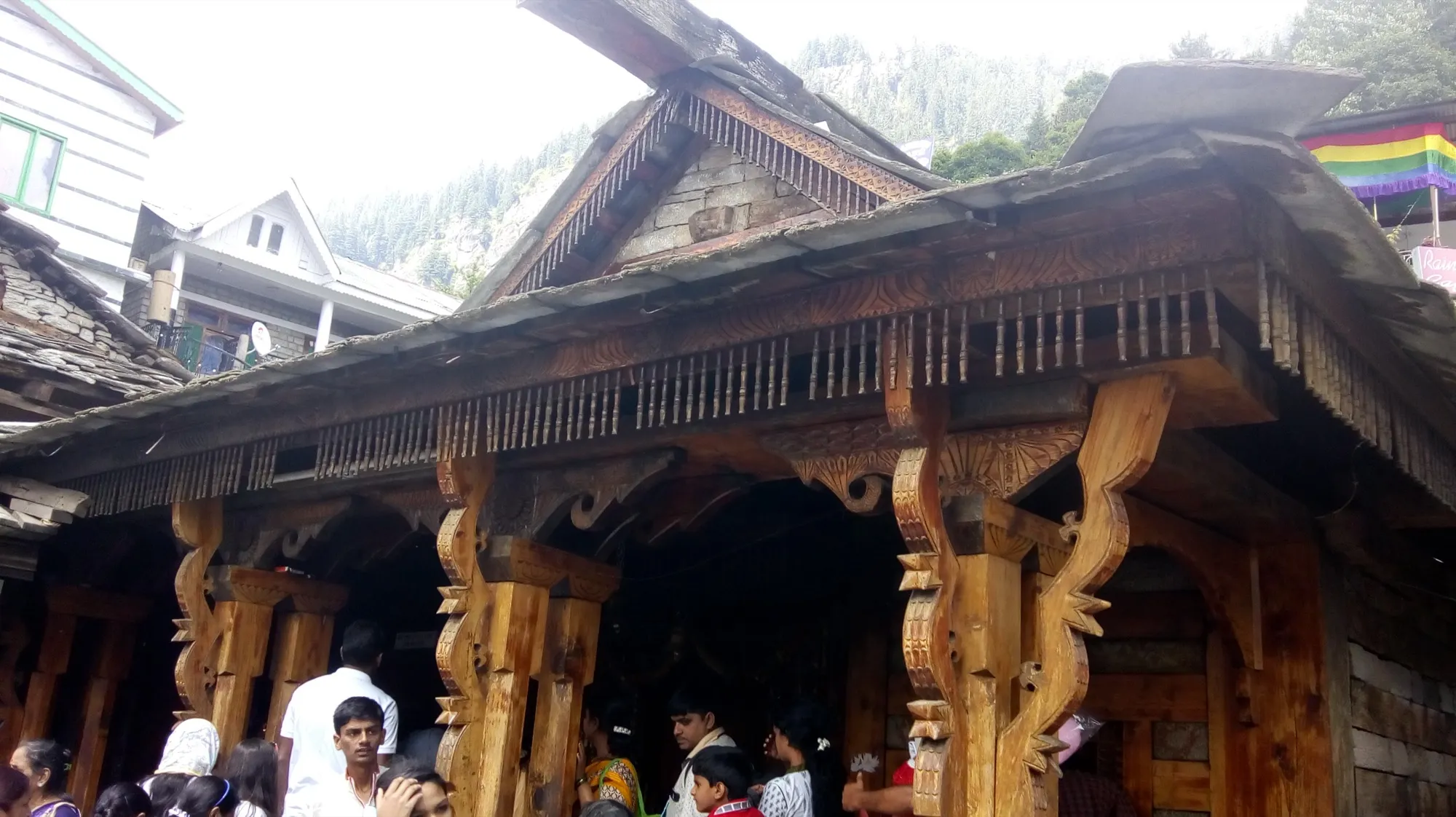 The carved wooden front of the Vashisht temple, with people at the entrance