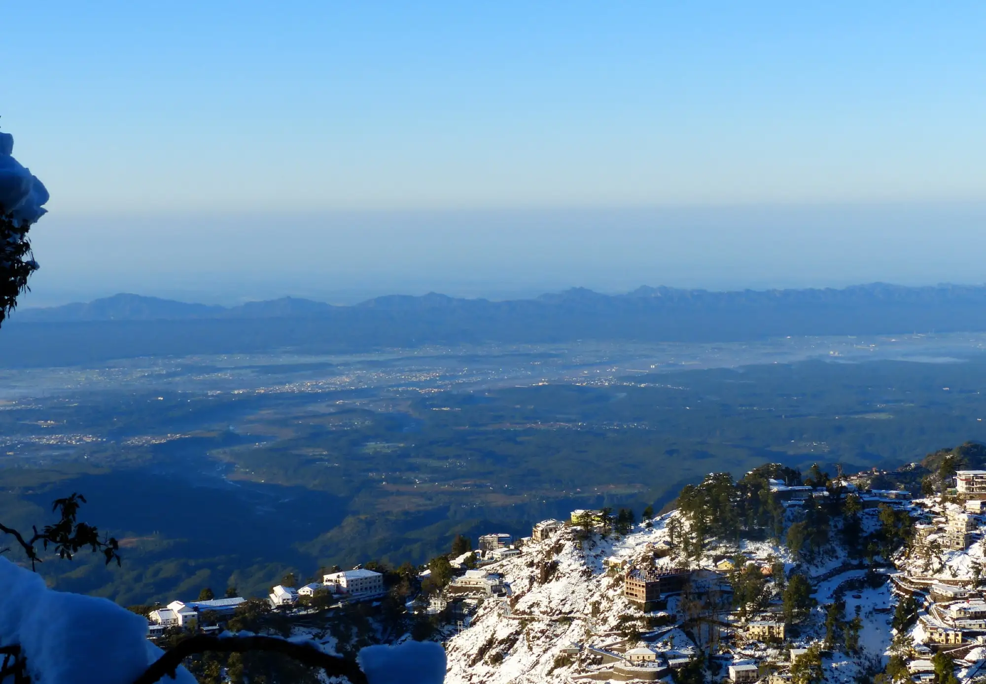 Snow on a hillside town above a hazy valley in Mussoorie
